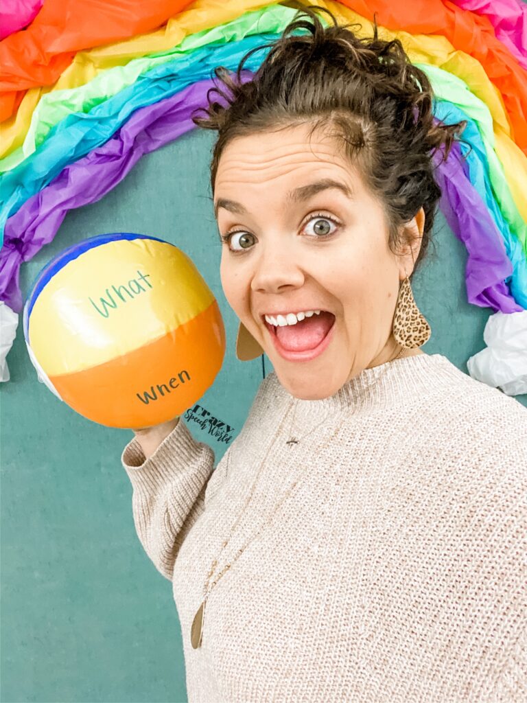 how to build rapport with students.  a woman is holding a beach ball, standing in front of a paper rainbow.  The beach ball has the words 'what' and 'when' written on it and she is smiling.